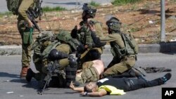 Israeli soldiers treat a wounded comrade after he was stabbed by a Palestinian, wearing a yellow vest, during clashes in the West Bank, Oct. 16, 2015. 