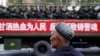 Một người đàn ông Uighur đứng nhìn một chiếc xe tải bán quân sự chở cảnh sát đi dọc theo một con đường trong một cuộc chống khủng bố.