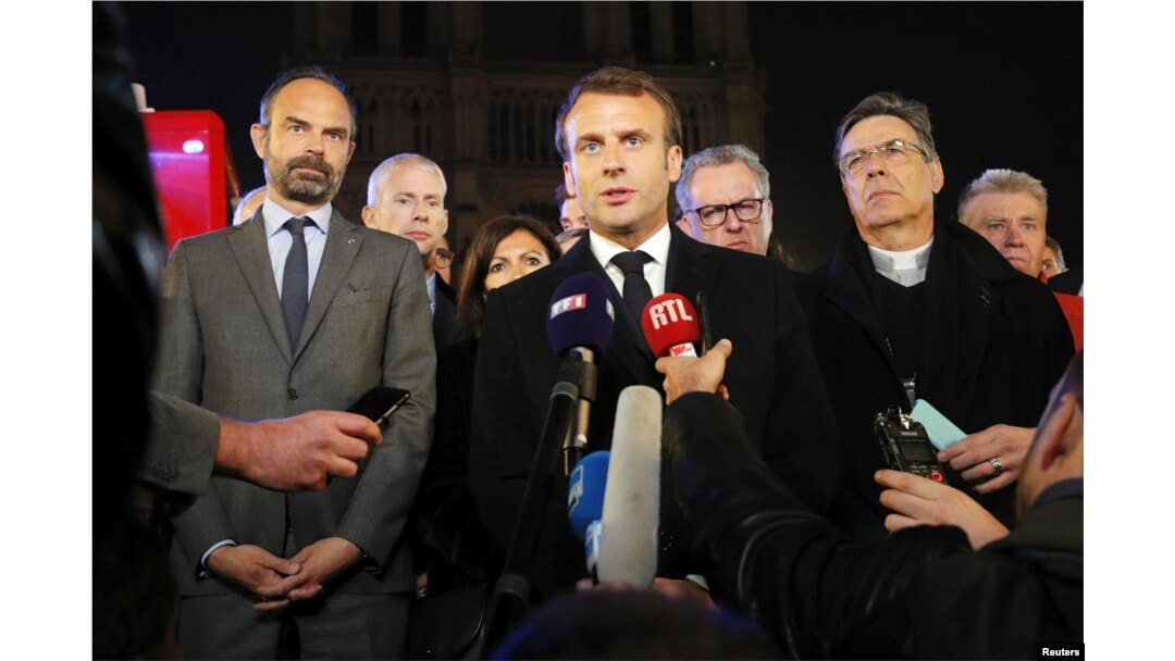 French President Emmanuel Macron speaks as Prime Minister Edouard Philippe and Archbishop of Paris, Michel Aupetit, stand near the Notre Dame Cathedral where a fire burns in Paris, France, April 15, 2019.