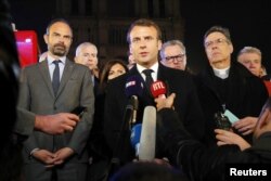 French President Emmanuel Macron speaks as Prime Minister Edouard Philippe and Archbishop of Paris, Michel Aupetit, stand near the Notre Dame Cathedral, France, Apr. 15, 2019.