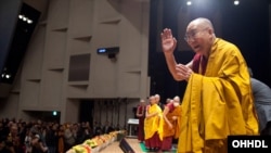 សម្តេច​សង្ឃ​ Dalai Lama កំពុង​បក់​ដៃ​ទៅ​កាន់​អ្នក​ចូលរួម​នៅ​ពេល​ចាប់​ផ្តើម​ថ្ងៃទី២​នៃ​ការ​បង្រៀន​របស់​ទ្រង់​នៅ​សាល Memorial Hall នៃ​សាកលវិទ្យាល័យ Showa Joshi Women's University ក្នុង​ក្រុង​តូក្យូ ប្រទេស​ជប៉ុន កាលពី​ថ្ងៃទី១៣ ខែមេសា ឆ្នាំ២០១៥។ 