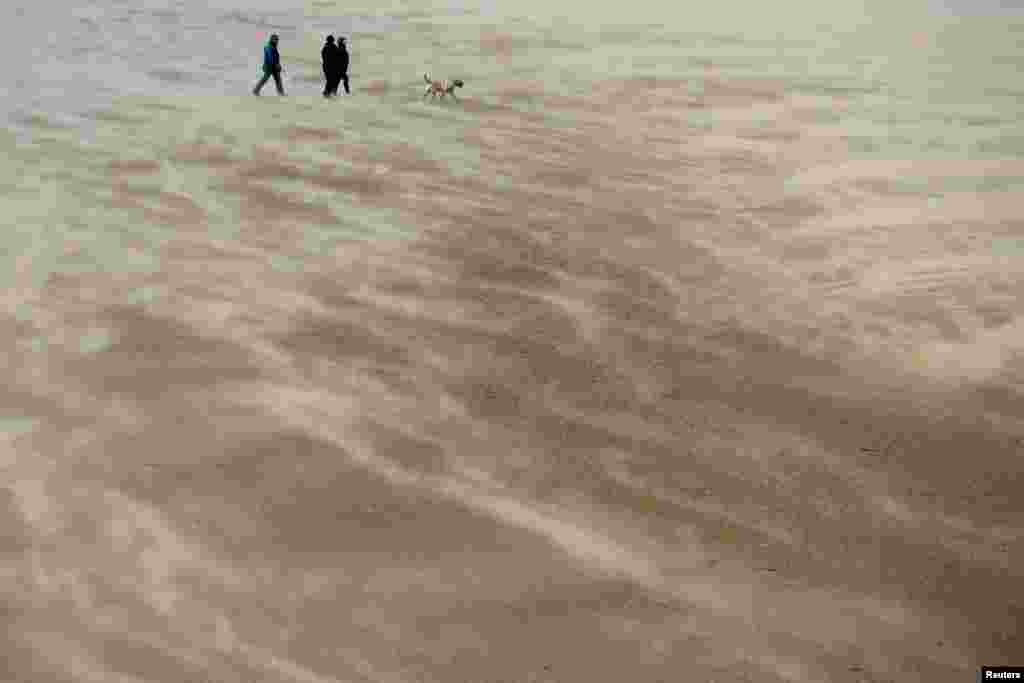 People walk along the beach through blowing sand in New Brighton, Britain.