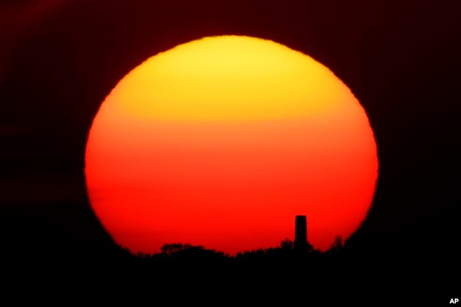 In this Friday, June 26, 2020 file photo, the sun sets behind a smokestack in the distance in Kansas City, Missouri. (AP Photo/Charlie Riedel, File)