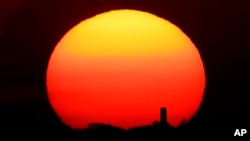 In this Friday, June 26, 2020 file photo, the sun sets behind a smokestack in the distance in Kansas City, Missouri. (AP Photo/Charlie Riedel, File)