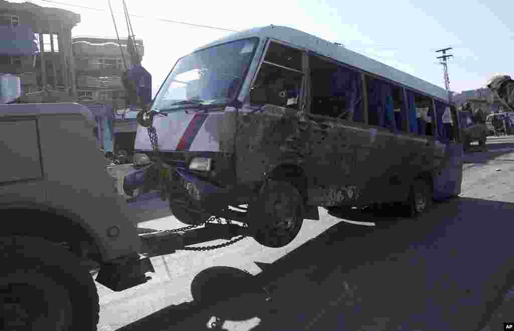 Afghan security forces tow away a mini bus which was destroyed in a roadside bomb explosion, in Kabul, Oct. 21, 2014. 