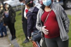 FILE - In this May 7, 2020 file photo, a pregnant woman wearing a face mask and gloves holds her belly as she waits in line for groceries at St. Mary's Church in Waltham, Mass. The Centers for Disease Control and Prevention urged all pregnant women Wednes