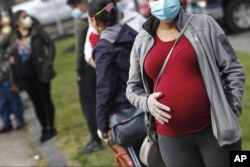 FILE - In this May 7, 2020 file photo, a pregnant woman wearing a face mask and gloves holds her belly as she waits in line for groceries at St. Mary's Church in Waltham, Mass. The Centers for Disease Control and Prevention urged all pregnant women Wednes