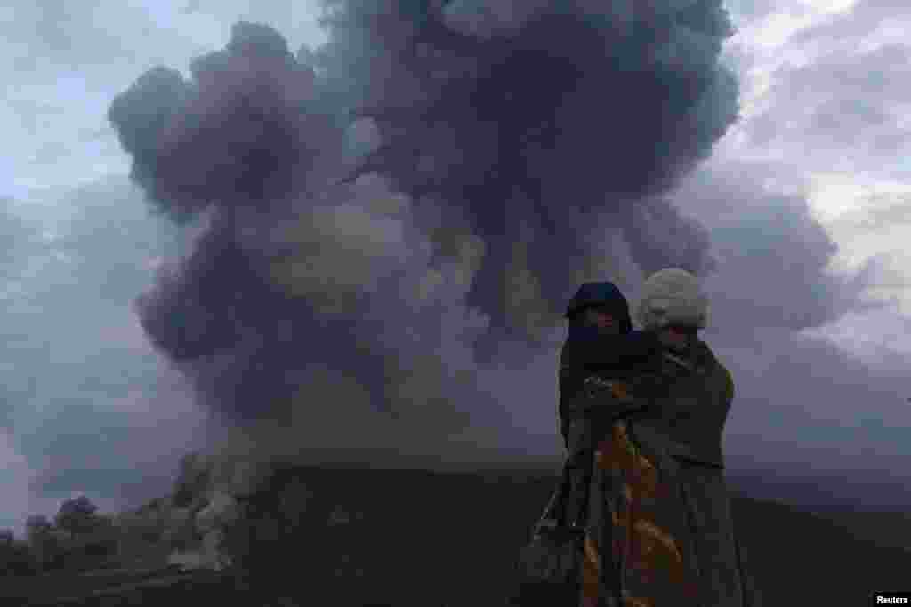 Seorang ibu memeluk anaknya, melihat letusan Gunung Sinabung di desa Berastepu, Kabupaten Karo, Provinsi Sumatera Utara. Lebih dari 22.000 warga di desa itu telah dievakuasi sejak pihak berwenang menaikkan status siaga ke tingkat yang paling tinggi untuk gunung berapi itu pada bulan November.