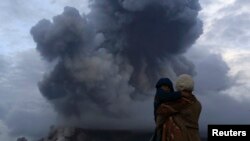 Seorang ibu dan anaknya menyaksikan letusan Gunung Sinabung dari desa Berastepu, kabupaten Karo, Sumatera Utara (10/1). (Reuters/Beawiharta)