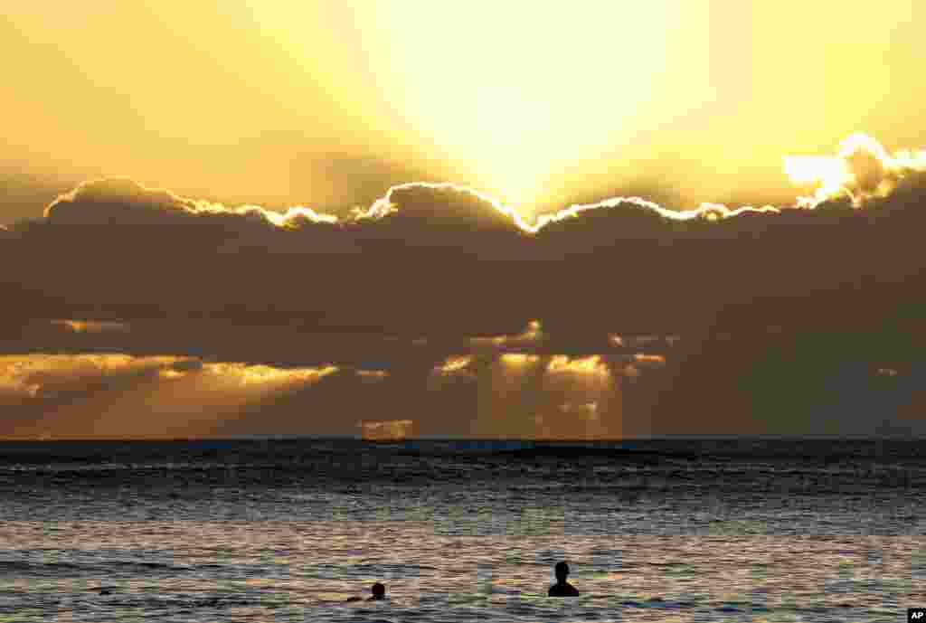 Sambil berenang, orang-orang menyaksikan matahari terbenam untuk terakhir kalinya pada tahun 2016, di Pantai Waikiki di Honolulu, Hawaii (31/12). (AP/Carolyn Kaster)