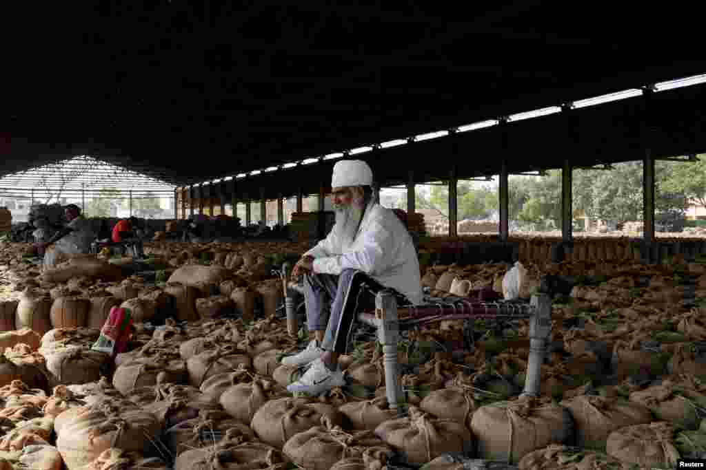 Seorang petani duduk di dipan kayu yang diletakkan di atas karung berisi hasil panen padi sambil menunggu pelanggan di pasar gandum di Karnal di negara bagian Haryana, India utara. (Reuters)&nbsp;