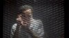 FILE - Egyptian photojournalist Mahmoud Abu Zeid, known by his nickname Shawkan, gestures in a soundproof glass cage inside a makeshift courtroom in Tora prison in Cairo, Egypt, July 28, 2018. 