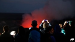 Visitors take pictures as Kilauea's summit crater glows red in Volcanoes National Park, Hawaii, May 9, 2018. Geologists warned Wednesday that Hawaii's Kilauea volcano could erupt explosively and send boulders, rocks and ash into the air around its summit in the coming weeks. 