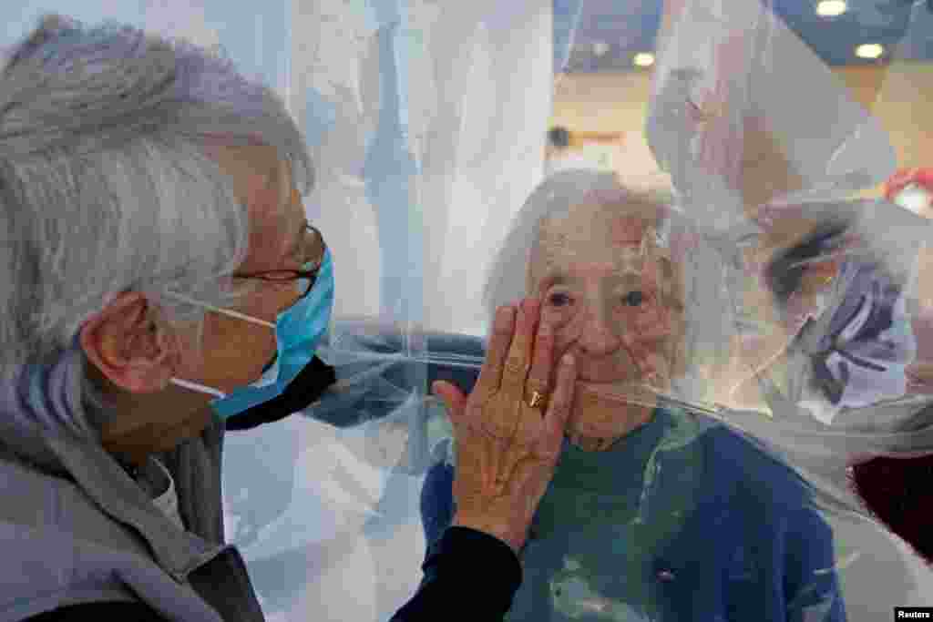 Two women speak with their 97-year-old mother behind a removable plastic sheet inside a bubble structure that lets families give hugs without risk of transmission of COVID-19, set up at Jeumont Hospital, in France.