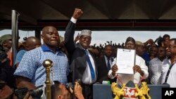 FILE - opposition politician Miguna Miguna, center, raises his fist as a gesture to the crowd as he stands next to opposition leader Raila Odinga, center-right, and politician James Orengo, far right, as Odinga holds an oath during a mock "swearing-in" ceremony at Uhuru Park in downtown Nairobi, Kenya, Jan. 30, 2018. 