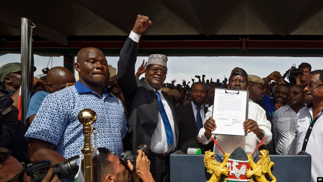 FILE - opposition politician Miguna Miguna, center, raises his fist as a gesture to the crowd as he stands next to opposition leader Raila Odinga, center-right, and politician James Orengo, far right, as Odinga holds an oath during a mock "swearing-in" ceremony at Uhuru Park in downtown Nairobi, Kenya, Jan. 30, 2018. 