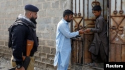 A worker from the National Database and Registration Authority, along with a police officer, verifies the identity cards of an Afghan citizen during a door-to-door search for undocumented Afghan nationals in Afghan Camp on the outskirts of Karachi, Pakistan, on Nov. 21, 2023.