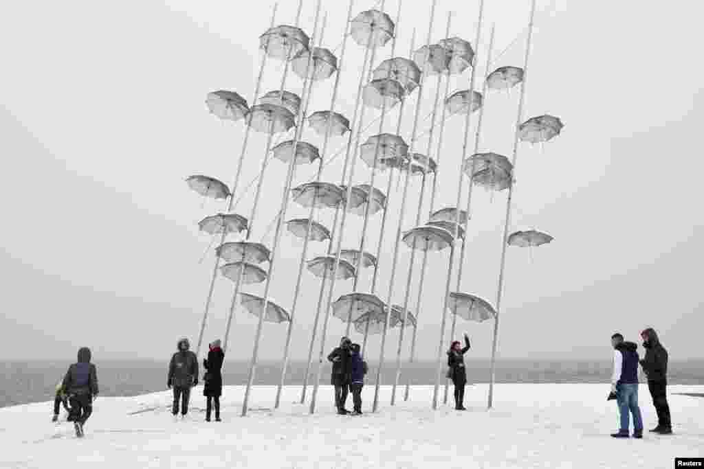 People take pictures next to the &quot;Umbrellas&quot; sculpture by famous Greek sculptor Giorgos Zogolopoulos, during a snowfall at the seaside walking path of Thessaloniki, Greece.