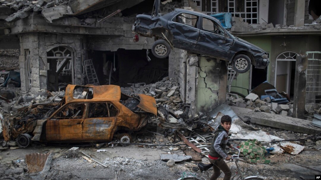 A boy rides his bike past destroyed cars and houses in a neighborhood recently liberated by Iraqi security forces, on the western side of Mosul, Iraq, Sunday, March 19, 2017. 