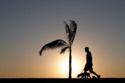 A man walks his dog as the sun sets in Asuncion, Paraguay, Aug. 1, 2020, amid the novel coronavirus pandemic.