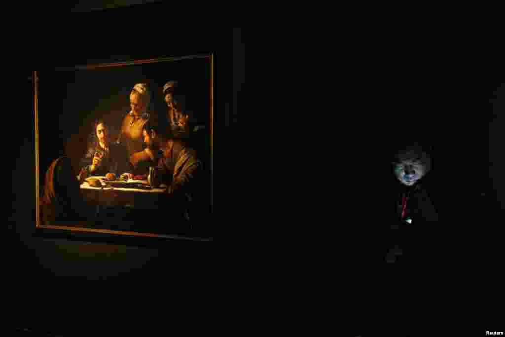 Một nhân viên an ninh xem điện thoại di động của mình bên cạnh bức &ldquo;Bữa ăn tối ở Emmaus,&#39; một kiệt tác hội họa phong cách Baroque của họa sĩ Ý Caravaggio, sau khi nó đã được treo tại một thư viện ở Hồng Kông.