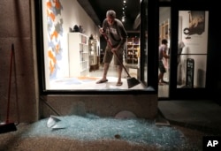 Scott McRoberts helps clean up broken glass after a violent crowd broke windows of many businesses after clashing with police, Sept. 16, 2017, in University City, Mo. Earlier, protesters marched peacefully in response to a not guilty verdict in the trial