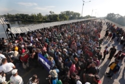 Migrants line up behind a Honduran flag at the border crossing between Guatemala and Mexico in Tecun Uman, Guatemala, Jan. 18, 2020.