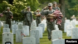 Soldiers salute as "Taps" is played during a military funeral nearby as they were placing flags on graves at Arlington National Cemetery in Virginia May 23, 2013.