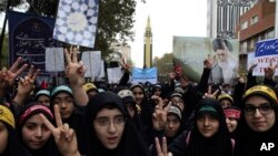 Anak-anak sekolah di Teheran, Iran, mengacungkan tanda kemenangan dalam pertemuan tahunan di depan bekas Kedutaan Besar AS yang menandai ulang tahun pengambilalihan tahun 1979, sementara Garda Revolusi memamerkan misil dalam pawai di belakangnya, Sabtu, 4 November 2017.