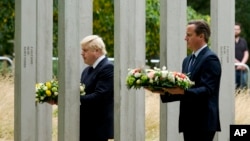 El primer ministro británico, David Cameron, derecha, y el alcalde de Londres, Boris Johnson, caminan hacia el memorial del 7/7 en Hyde Park en Londres para colocar ofrendas florales, el martes, 7 de julio de 2015.
