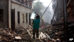 A Nepalese man carrying a water jar walks past damaged houses in Bhaktapur, Nepal, May 14, 2015. 