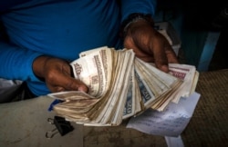 FILE - A worker shows a wad of Cuban pesos in Havana, Cuba, Dec. 11, 2020.