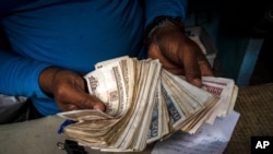 FILE - A worker shows a wad of Cuban pesos in Havana, Cuba, Dec. 11, 2020.