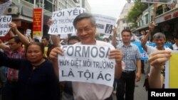 FILE - Political dissident Nguyen Quang A (C) holds a sign which reads "Formasa - damaged the environment and is a criminal" during a protest in Hanoi, Vietnam, May 1, 2016.