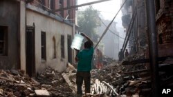 A Nepalese man carrying a water jar walks past damaged houses in Bhaktapur, Nepal, May 14, 2015. 