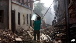 FILE - A Nepalese man carrying a water jar walks past damaged houses in Bhaktapur, Nepal, May 14, 2015. 