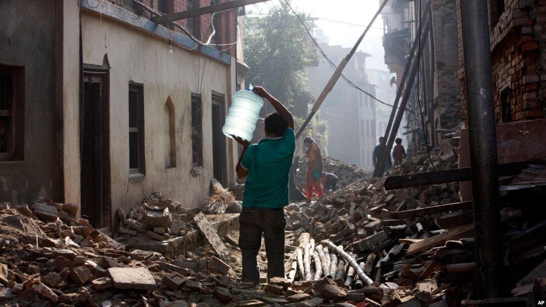 A Nepalese man carrying a water jar walks past damaged houses in Bhaktapur, Nepal, May 14, 2015. 