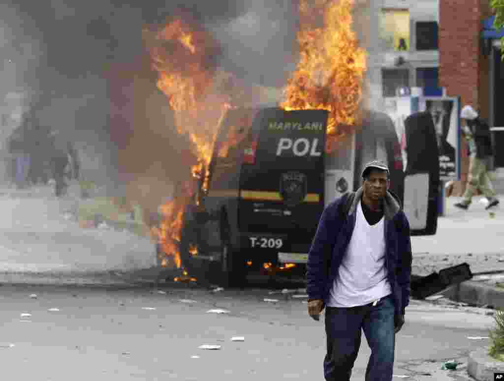 A man walks past a burning police vehicle, April 27, 2015, during unrest following the funeral of Freddie Gray in Baltimore.