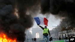 A demonstrator waves the French flag onto a burning barricade on the Champs-Elysees avenue with the Arc de Triomphe in background, during a demonstration against the rising of the fuel taxes, Saturday, Nov. 24, 2018 in Paris.