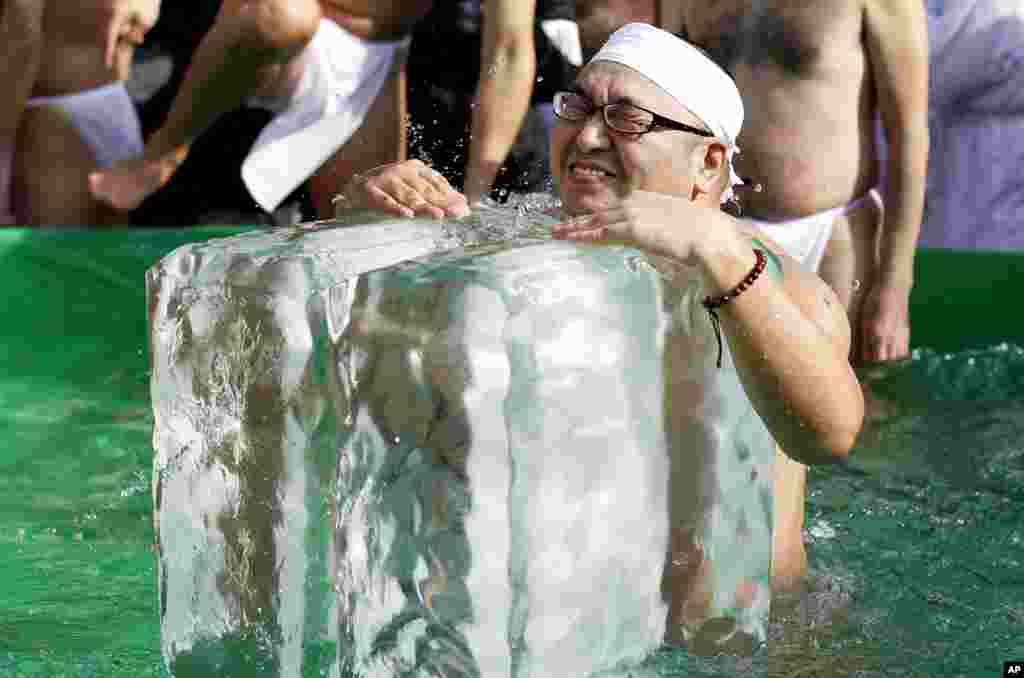 A Japanese physical fitness enthusiast touches a large ice cube while dipping in icy water with others during a winter ritual to keep themselves fit and display their perseverance at Teppozu Inari Shinto Shrine in Tokyo.