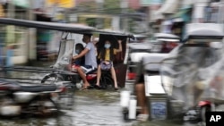 Warga yang memakai masker untuk mencegah penyebaran virus corona naik sepeda motor saat melewati jalan yang banjir akibat Topan Molave di Provinsi Pampanga, Filipina utara, 26 Oktober 2020, sebagai ilustrasi. (Foto: AP)