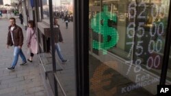 FILE - People walk past an exchange office screen showing the currency exchange rates, in Moscow, Russia, April 10, 2018. 