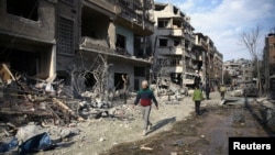 People walk past bombed-out buildings after an air raid in the besieged town of Douma, east of Damascus, Syria, Feb. 23, 2018.