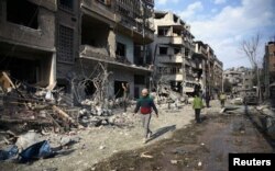 People walk through the damage, after an air raid in the besieged town of Douma, Eastern Ghouta, Damascus, Syria, Feb. 23, 2018.