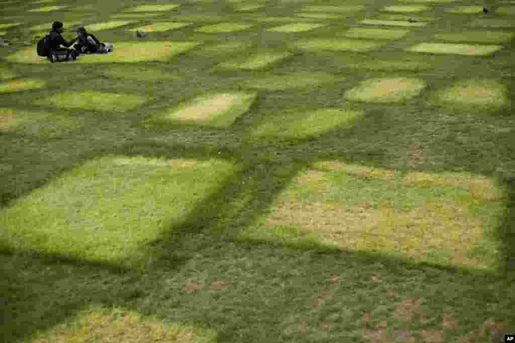 People sit eating next to tent marks outlined on grass where Extinction Rebellion climate protesters had set up a camp in Marble Arch, London, England.