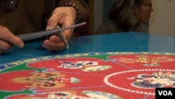 Mandala artist Losang Samten is dispensing sand using metal tools called Chatpur, which he has been using for more than 30 years to create mandalas. (VOA/ J. Soh)