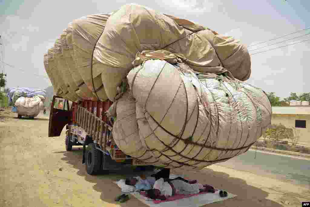 Men sleep in the shadow of an overflowing cloth container of hay on a truck on a hot summer day in Ajmer in the western state of Rajasthan, India.