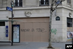 The words "Give back the money" are written on the facade of a bank in Paris, Dec. 15, 2018, as protesters wearing yellow vests arrive to demonstrate against rising costs of living they blame on high taxes.