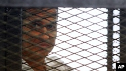Wartawan Al Jazeera Peter Greste melihat dari balik kurungan besi saat menghadiri sidang di pengadilan Kairo, Mesir, 23 Juni 2014 (Foto: dok).
