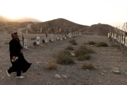 A woman walks past graves at a Hazara cemetery for the Shiite community martyrs on a hill on the outskirts of Kabul, Oct. 20, 2021.